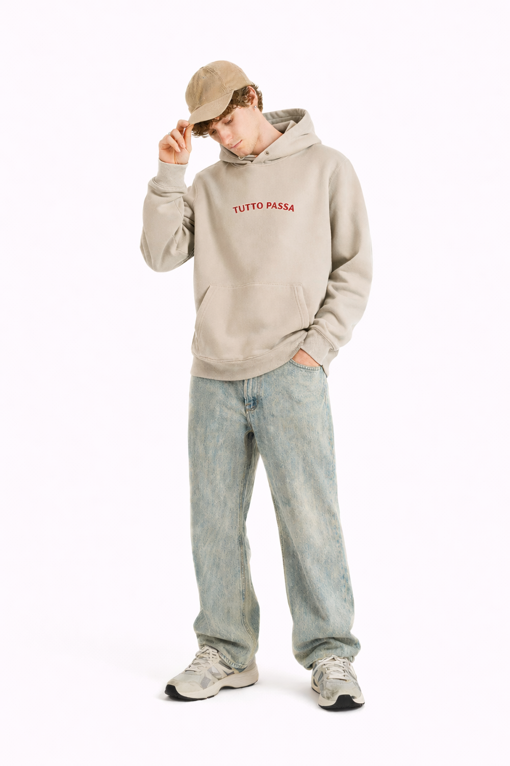 Person wearing a beige hoodie with text, light blue jeans, and a cap on a white background