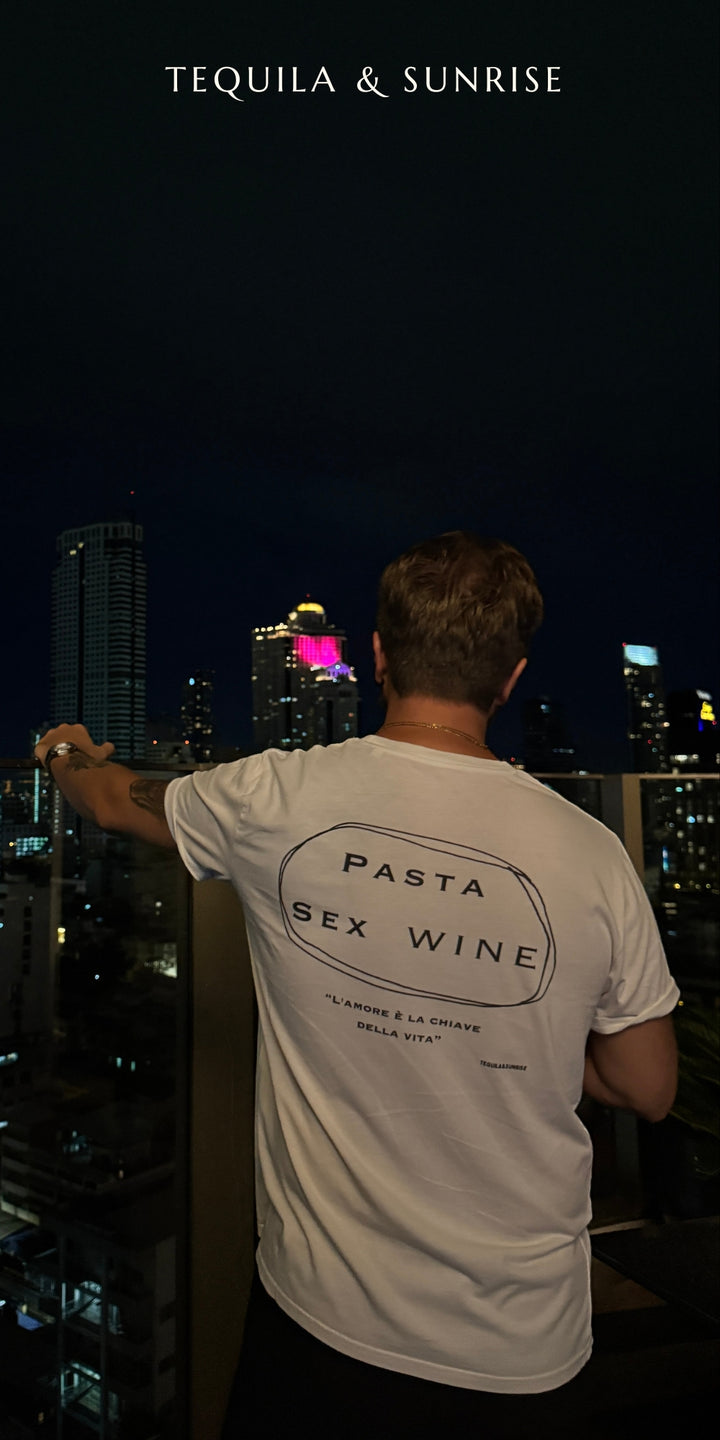 Man wearing Pasta & Sex & Wine Organic T-shirt against a city skyline at night.