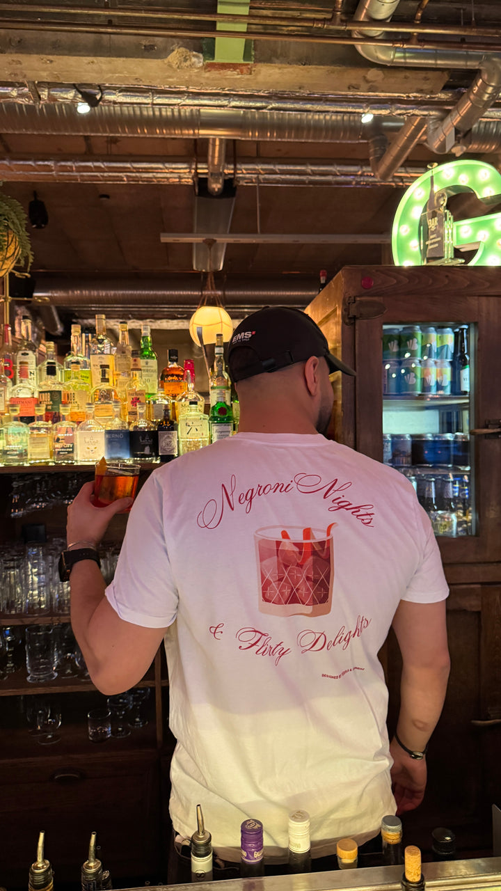 Person wearing a Negroni Nights & Flirty Delights Organic T-shirt in a bar, holding a drink.