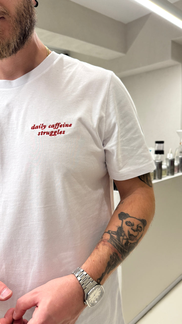 Close-up of a man wearing the Daily Caffeine Struggles Organic T-shirt, featuring coffee-themed text.