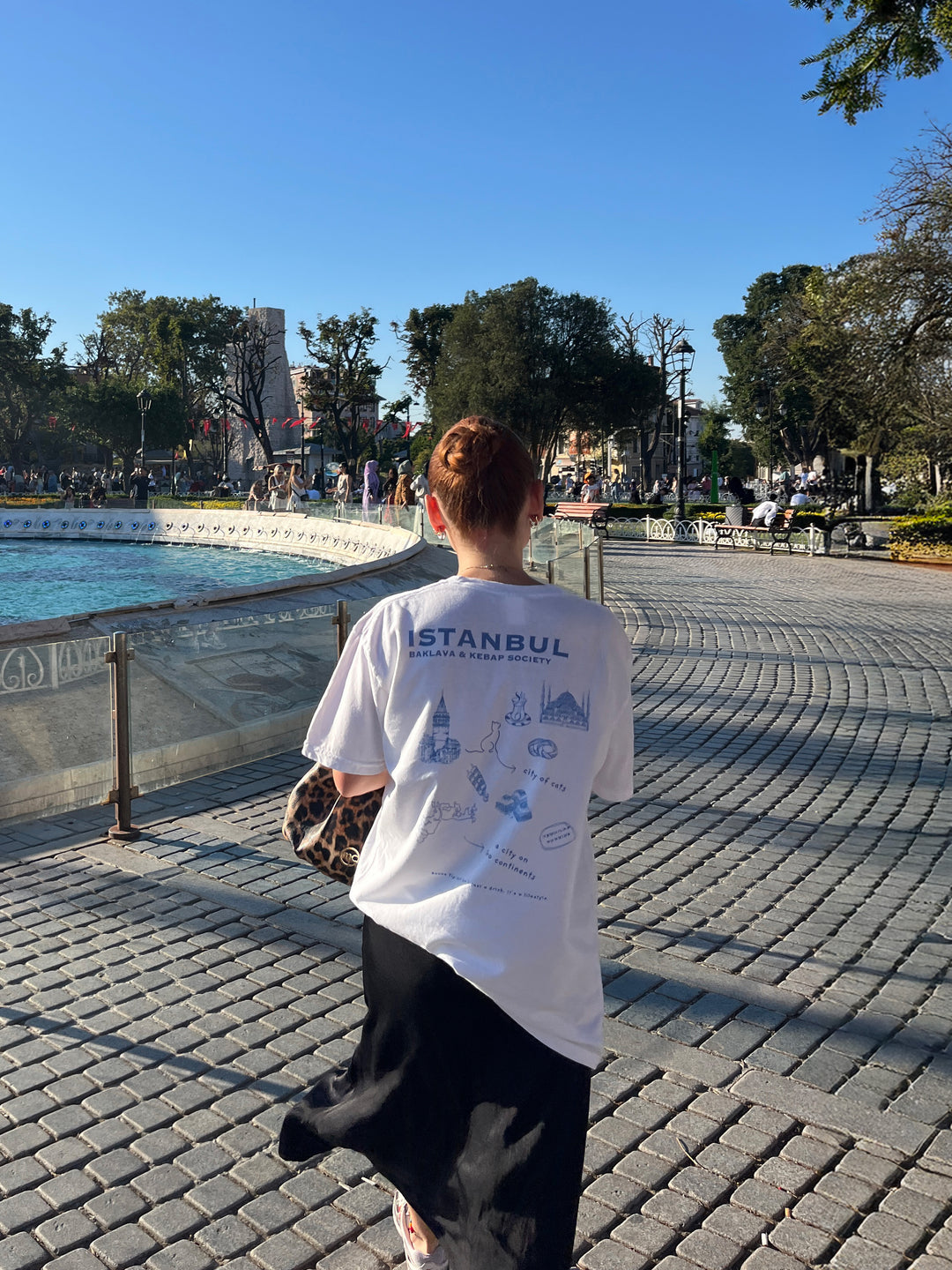 Woman wearing Istanbul Baklava & Kebab Society Organic T-shirt by a fountain in Istanbul.