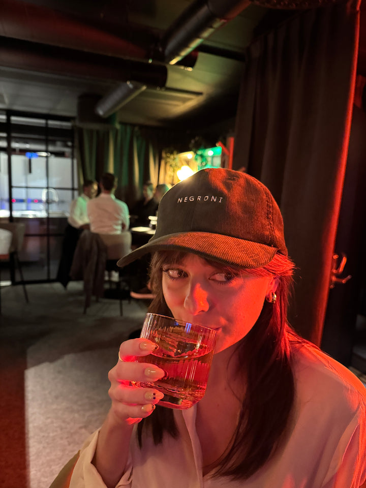 Person holding a negroni glass with a blurred indoor background
