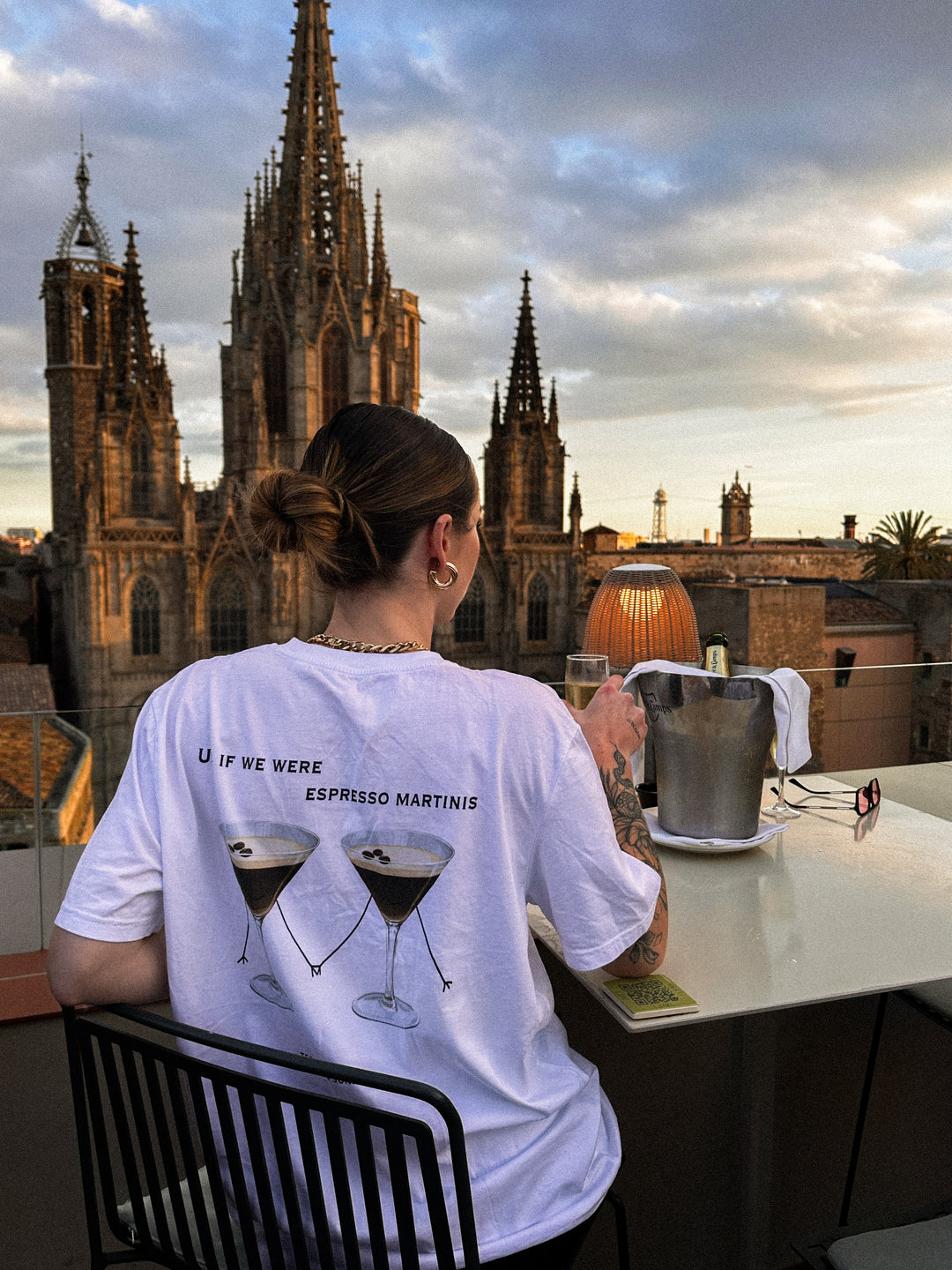 Person wearing If We Were Espresso Martinis Organic T-shirt with city skyline background.