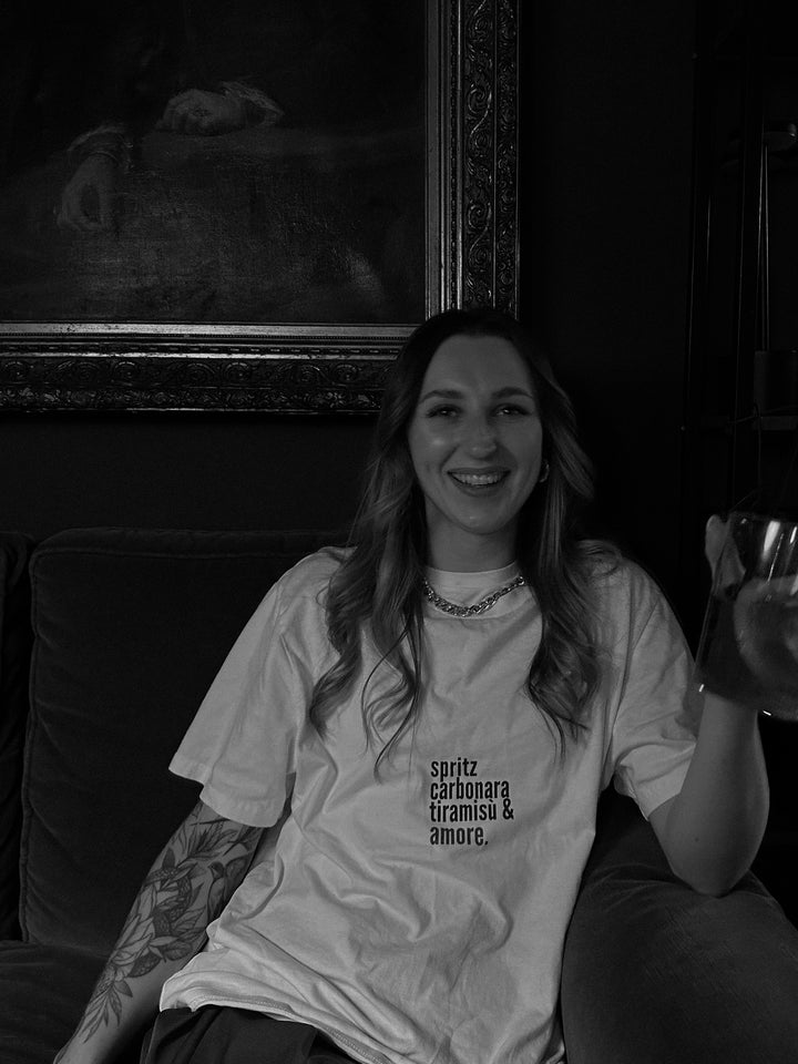 A person wearing a Love from Italy Organic T-shirt featuring Italian dish themes, sitting on a couch.