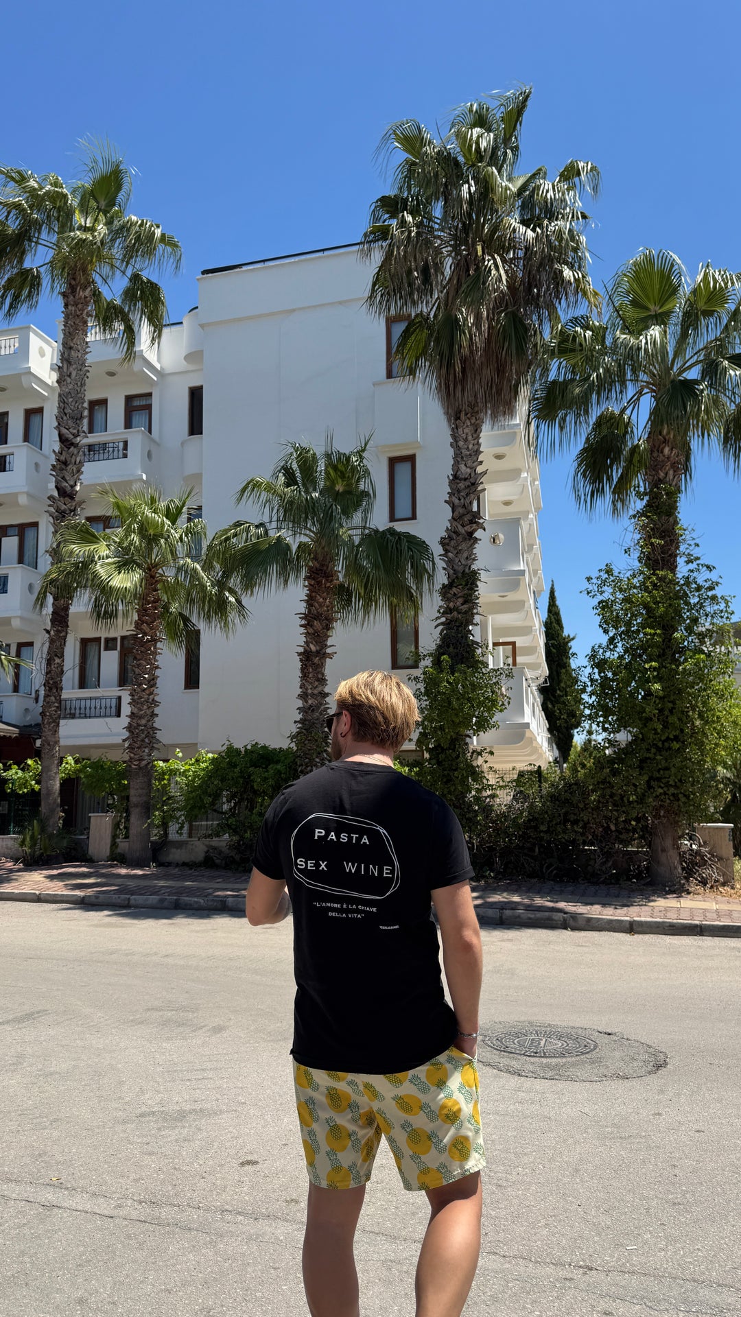 Man wearing Pasta & Sex & Wine Organic T-shirt in a sunny location with palm trees.