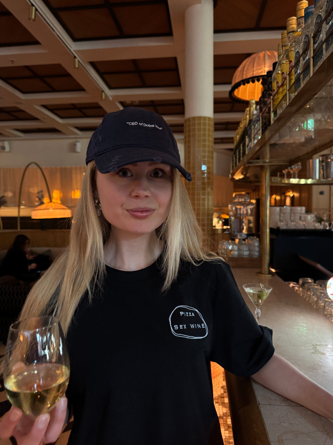 Model wearing a Pizza & Sex & Wine Organic T-shirt and holding a glass of wine in a stylish bar.