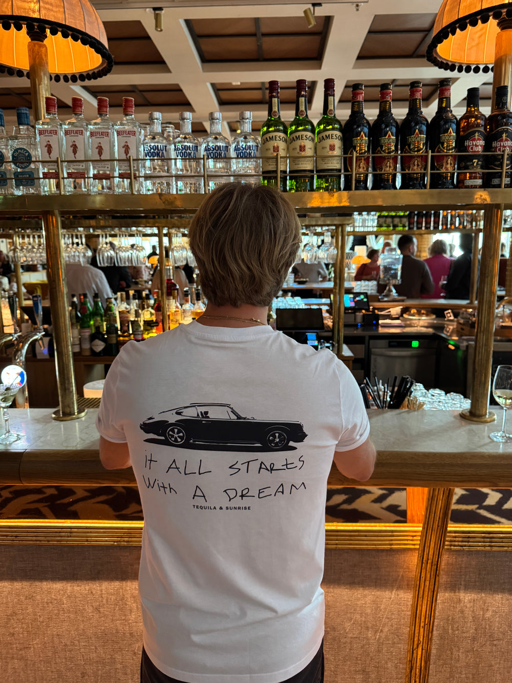 The It All Starts with a Dream Organic T-shirt displayed in a bar setting with a bartender behind the bar.