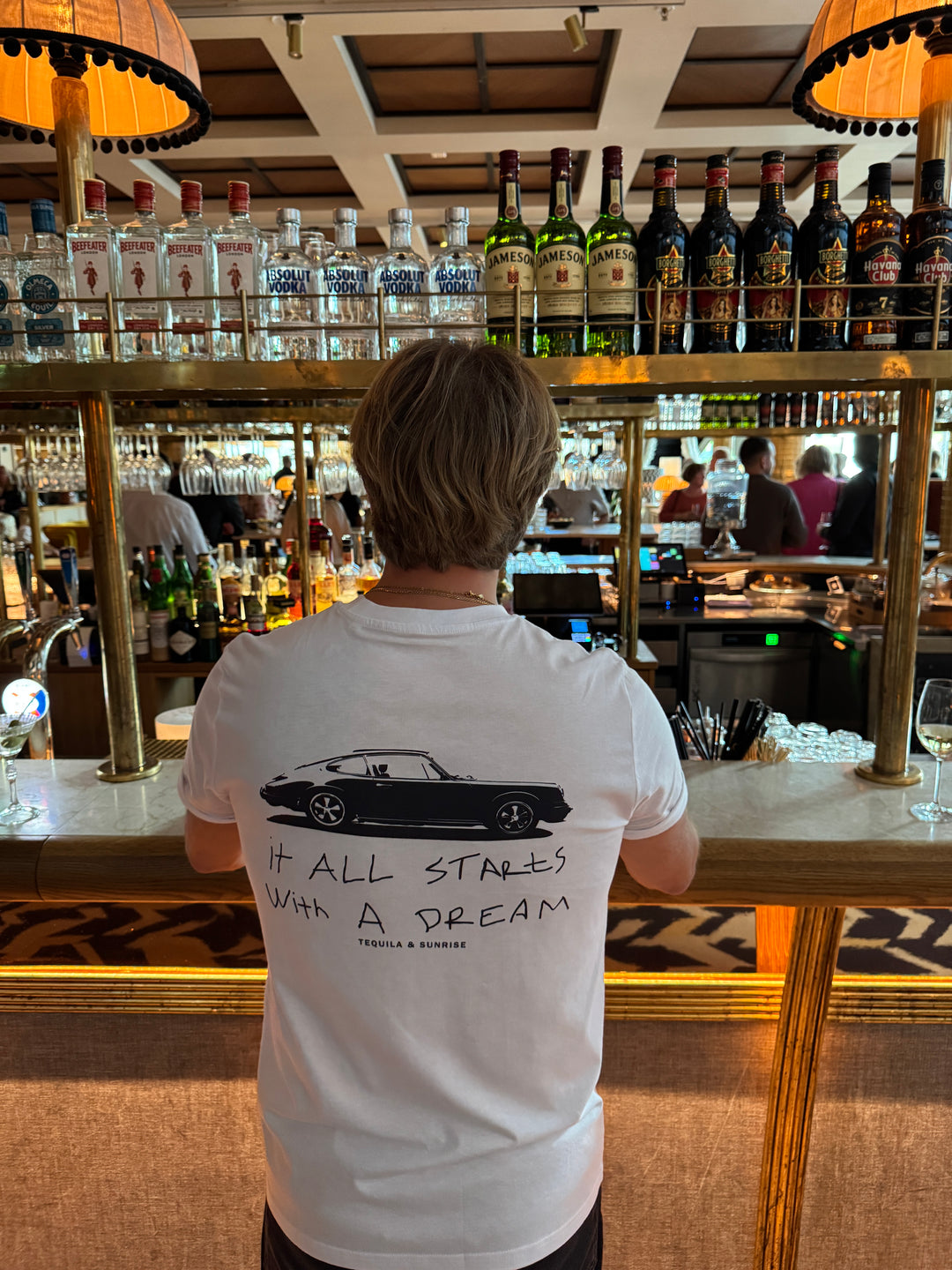 The It All Starts with a Dream Organic T-shirt displayed in a bar setting with a bartender behind the bar.