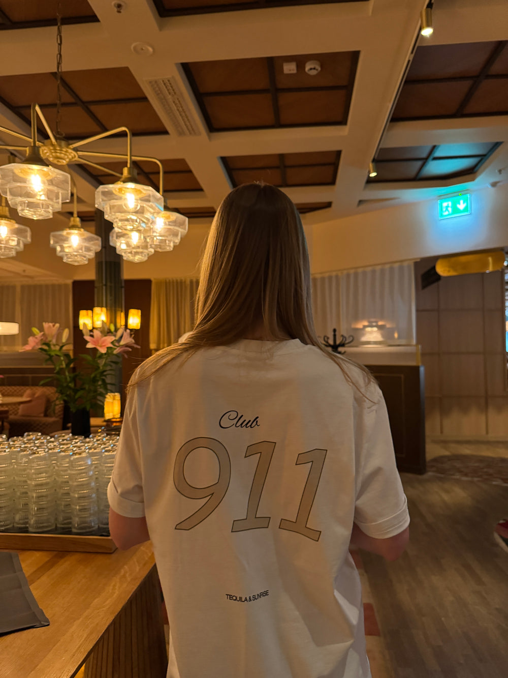 Person wearing a Porsche Club 911 Organic T-shirt in an elegant interior setting.