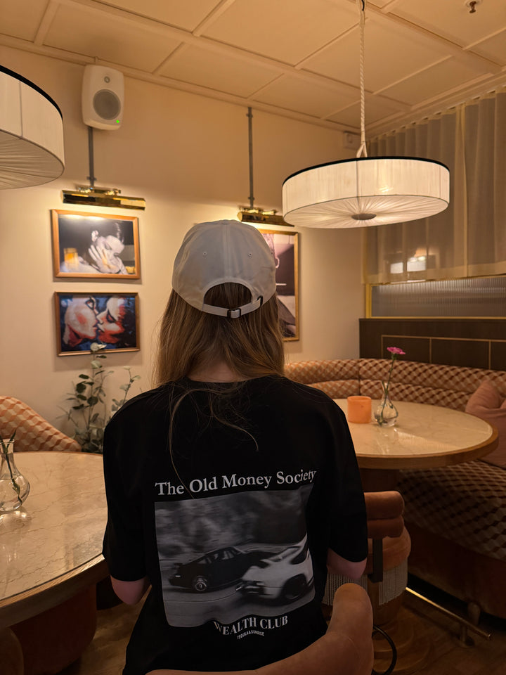 A person wearing an Old Money Society Organic T-shirt in a stylish indoor setting.