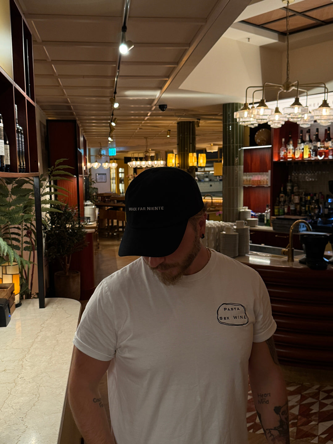 Man wearing a Pasta & Sex & Wine Organic T-shirt in a stylish restaurant interior.