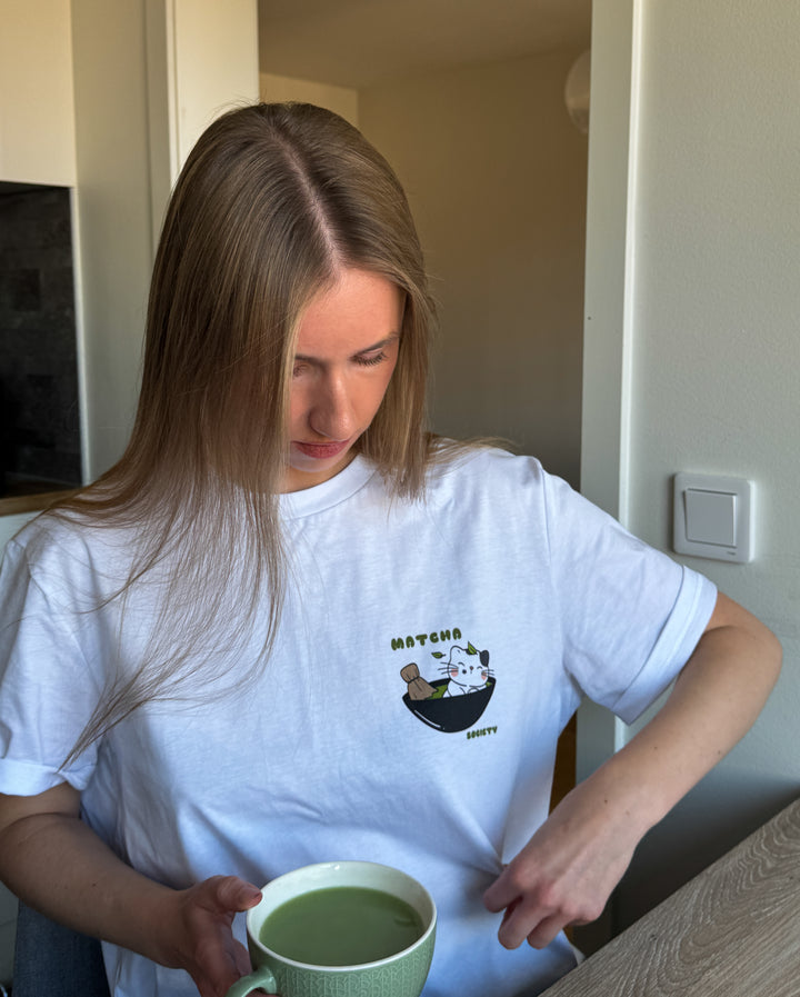 Woman in a white t-shirt holding a green mug in a room.