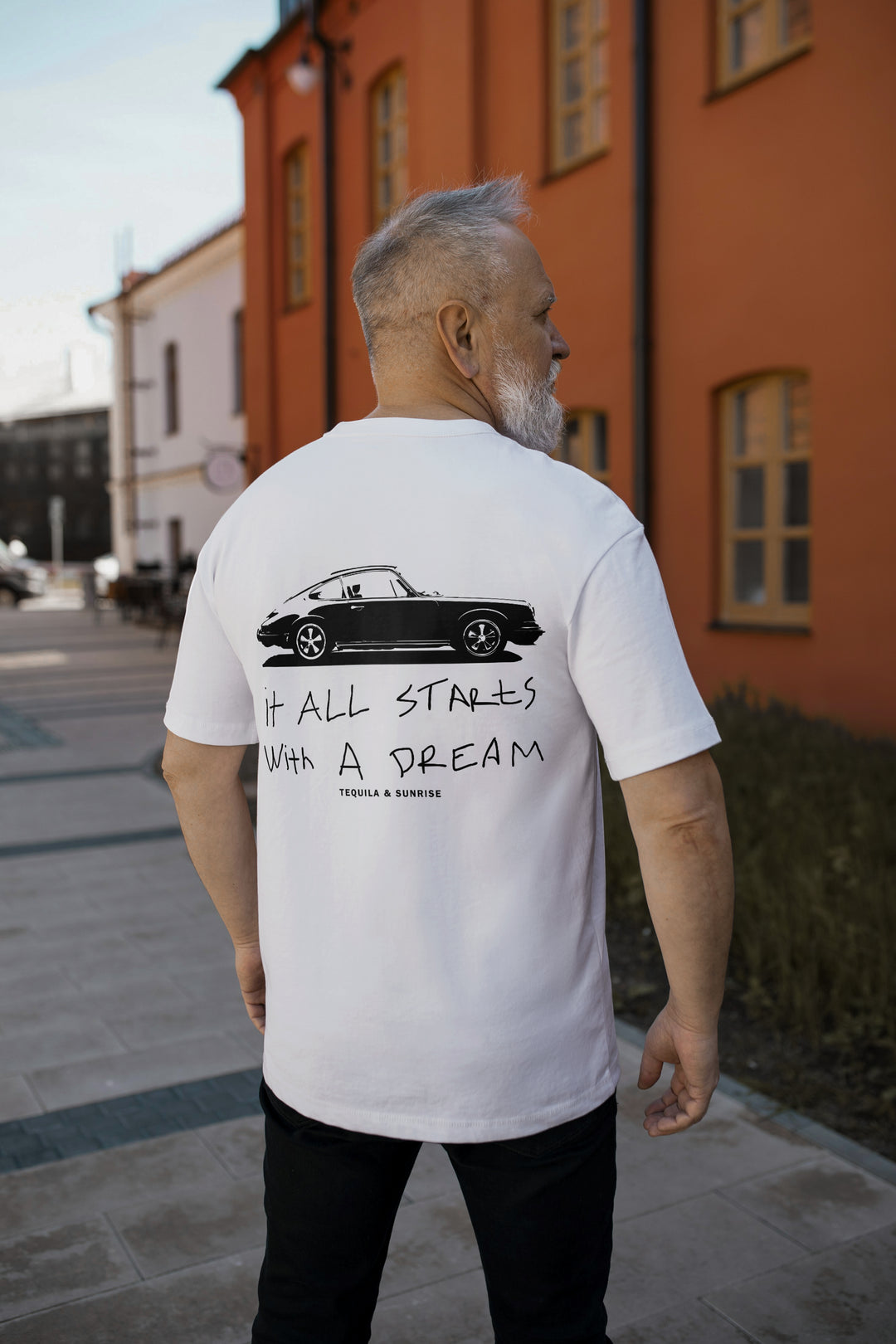 The It All Starts with a Dream Organic T-shirt displayed on a person outdoors, featuring a car graphic on the back.