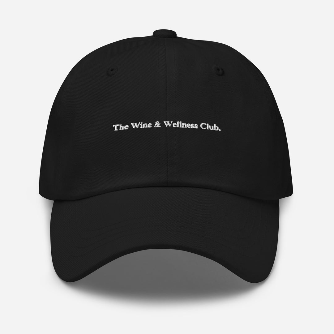 The Wine & Wellness Club by Tequila & Sunrise is a black black hat crafted from chino cotton twill, showcasing white text that reads "The Wine & Wellness Club." It features an adjustable strap for a perfect fit.