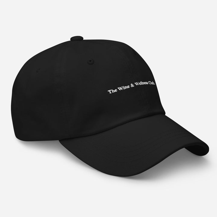 Side view of The Wine & Wellness Club by Tequila & Sunrise is a black navy hat crafted from chino cotton twill, showcasing white text that reads "The Wine & Wellness Club." It features an adjustable strap for a perfect fit.