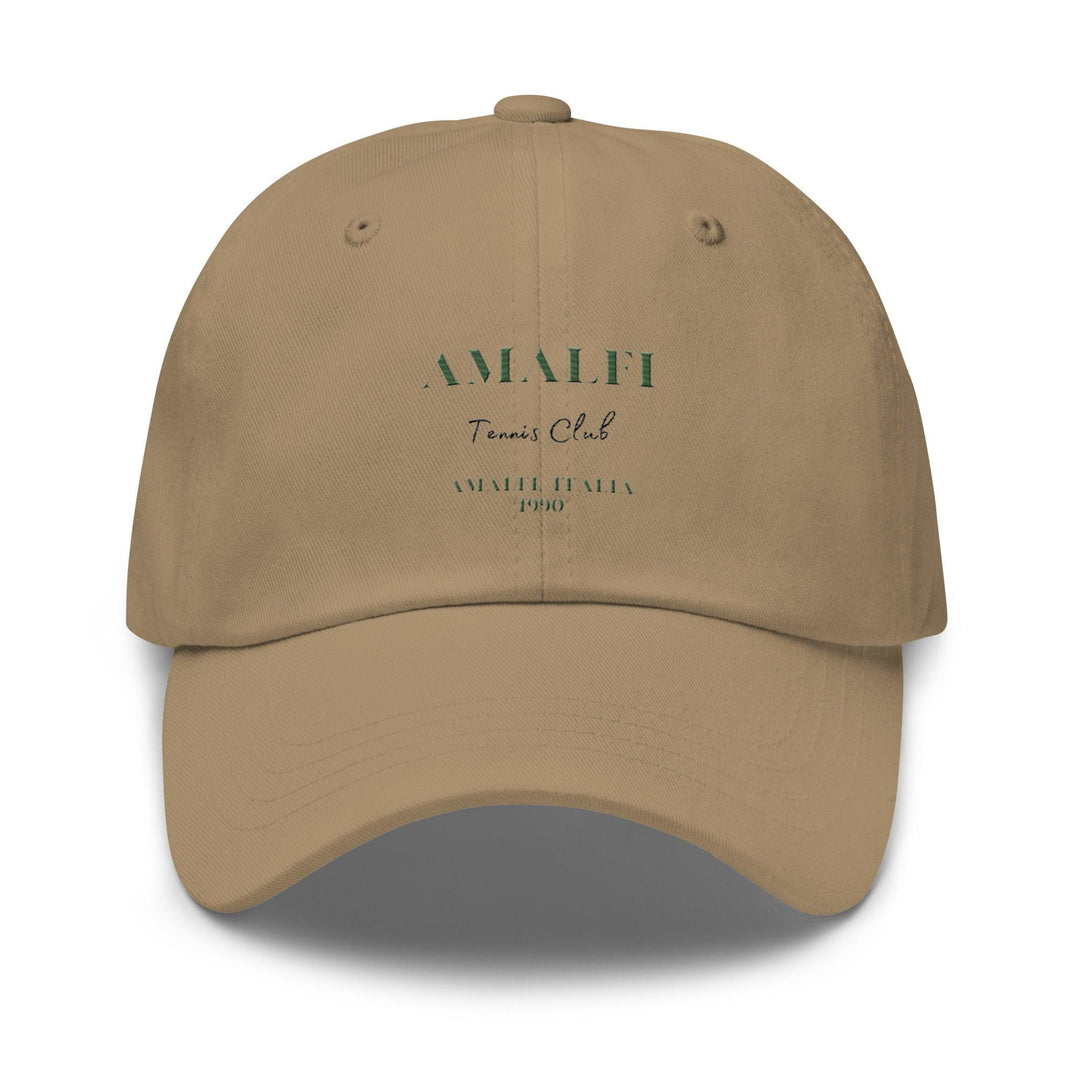 The Amalfi Tennis Club Italia Hat by Tequila & Sunrise is a beige baseball cap made from chino cotton twill, showcasing "AMALFI Tennis Club AMALFI, ITALIA 1990" printed in green and black on the front. This classic Dad hat includes an adjustable strap for a perfect fit.