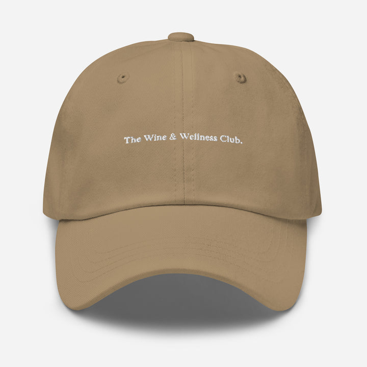 The Wine & Wellness Club by Tequila & Sunrise is a khaki hat crafted from chino cotton twill, showcasing white text that reads "The Wine & Wellness Club." It features an adjustable strap for a perfect fit.