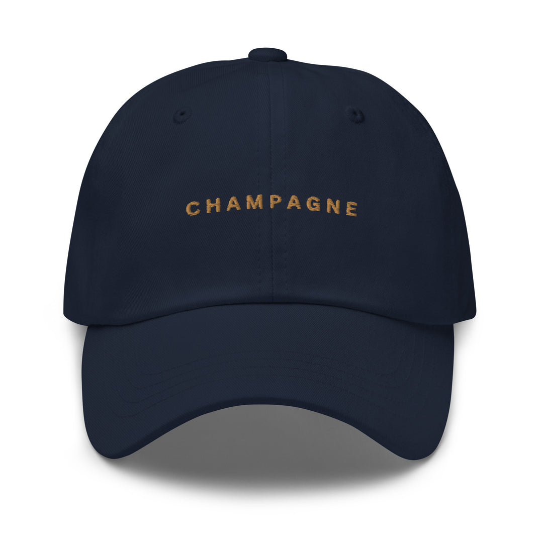 The Champagne Dad Hat by Tequila & Sunrise is a navy blue baseball cap made from chino cotton twill, showcasing the word CHAMPAGNE embroidered in gold on the front. With its adjustable strap, this hat seamlessly blends style and comfort.