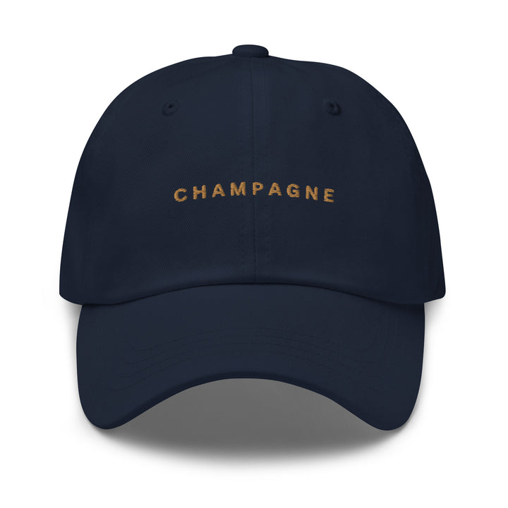 The Champagne Dad Hat by Tequila & Sunrise is a navy blue baseball cap made from chino cotton twill, showcasing the word CHAMPAGNE embroidered in gold on the front. With its adjustable strap, this hat seamlessly blends style and comfort.