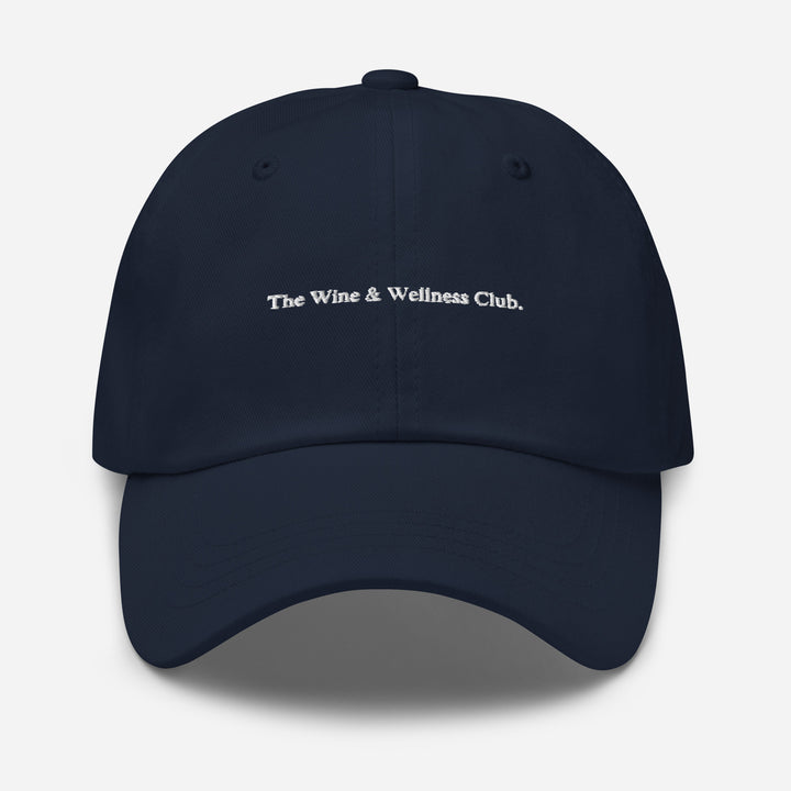 The Wine & Wellness Club by Tequila & Sunrise is a black navy hat crafted from chino cotton twill, showcasing white text that reads "The Wine & Wellness Club." It features an adjustable strap for a perfect fit.