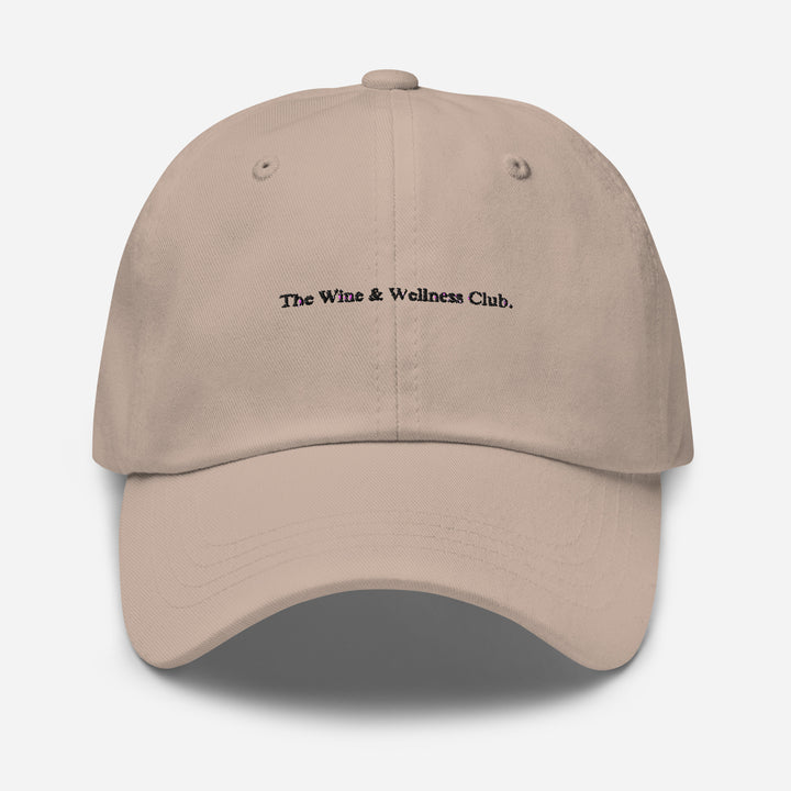 The Wine & Wellness Club by Tequila & Sunrise is a stone hat crafted from chino cotton twill, showcasing black text that reads "The Wine & Wellness Club." It features an adjustable strap for a perfect fit.