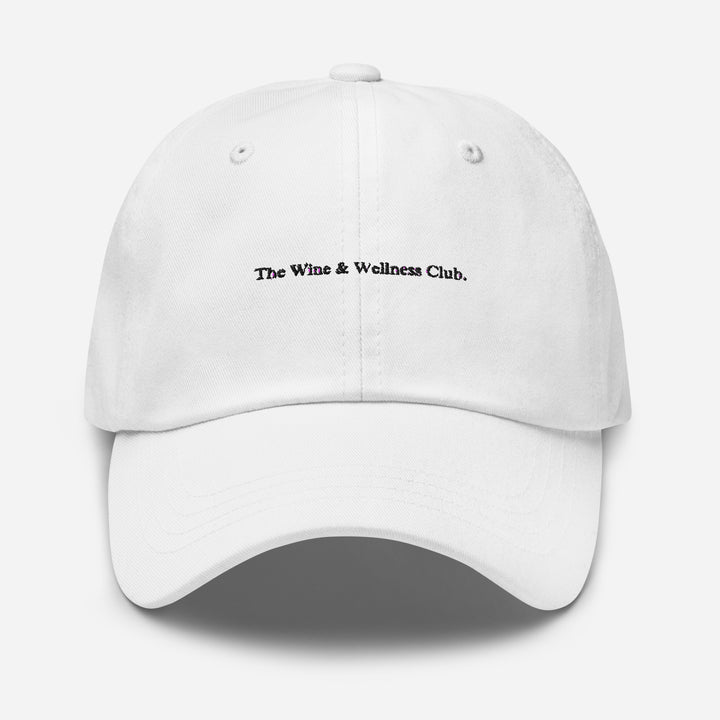 The Wine & Wellness Club by Tequila & Sunrise is a white hat crafted from chino cotton twill, showcasing black text that reads "The Wine & Wellness Club." It features an adjustable strap for a perfect fit.