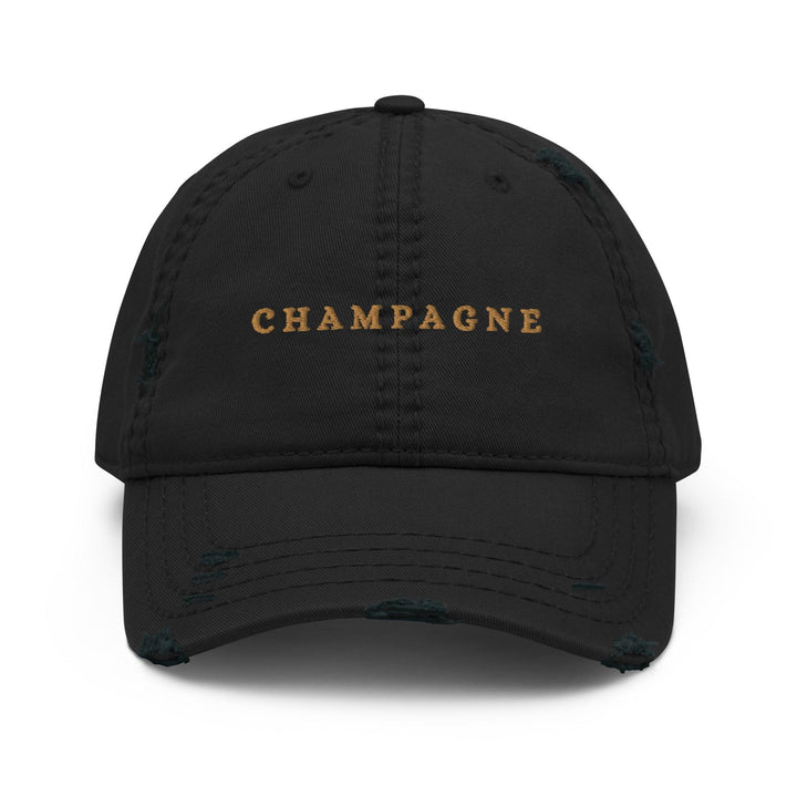 The Champagne Hat by Tequila & Sunrise showcases the word CHAMPAGNE beautifully embroidered in gold on its front, complementing the hat's black, distressed design. It's an ideal addition to any sophisticated wardrobe.