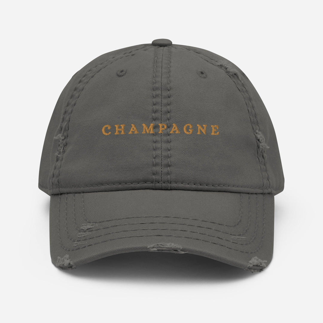 The Champagne Hat by Tequila & Sunrise is a green dad hat with distressed edges, featuring the word CHAMPAGNE embroidered in gold on the front, making it perfect for adding a touch of flair to a sophisticated wardrobe.