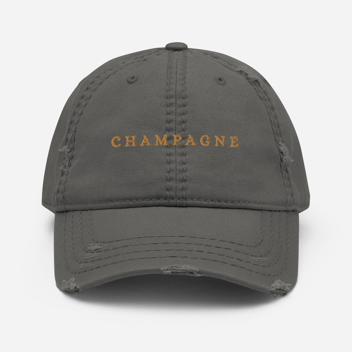 The Champagne Hat by Tequila & Sunrise is a green dad hat with distressed edges, featuring the word CHAMPAGNE embroidered in gold on the front, making it perfect for adding a touch of flair to a sophisticated wardrobe.