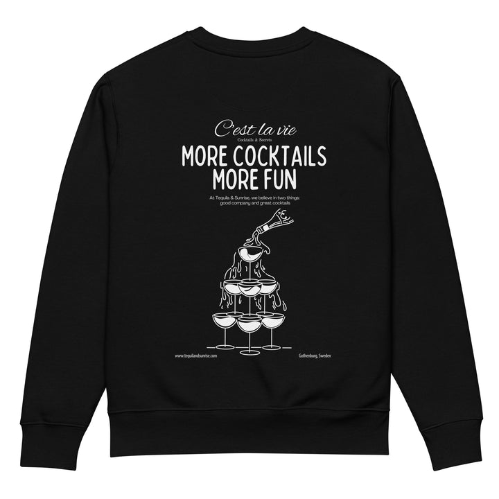 The More Cocktails More Fun Eco Sweatshirt by Tequila & Sunrise is a unisex design crafted from organic cotton. It showcases a black color with a white graphic of a champagne tower being poured and features the text "C'est la vie" and "More Cocktails More Fun," encouraging wearers to relish good company and cocktails while supporting sustainable fashion.