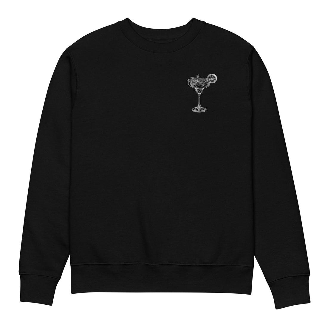 The "Mamacita Needs a Margarita" Eco Sweatshirt by Tequila & Sunrise is a black unisex garment featuring a small embroidered cocktail glass with garnish on the chest. Made from organic cotton, it combines sustainable fashion with stylish design.