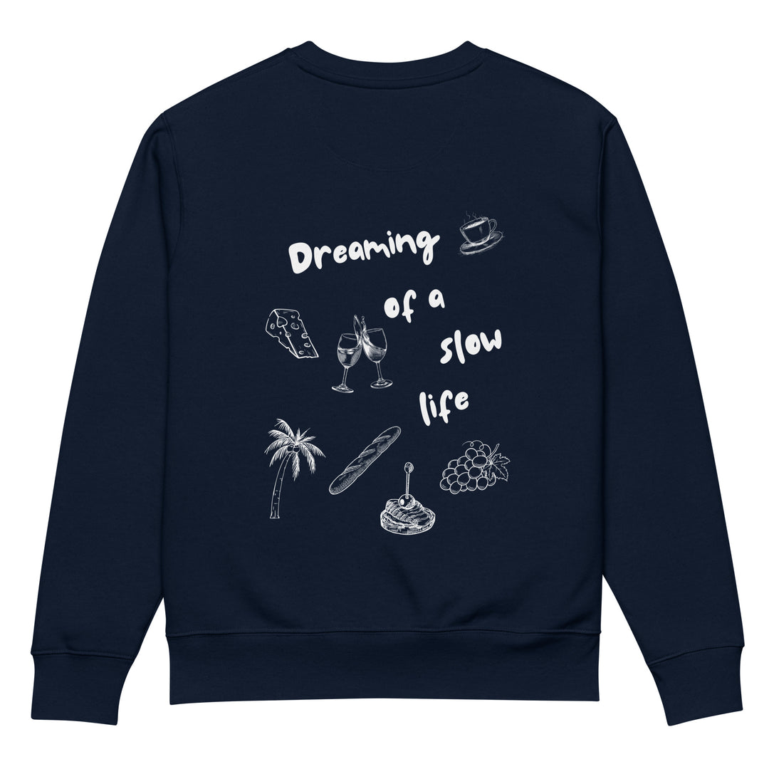 The La Vita Lenta Eco Sweatshirt by Tequila & Sunrise is a navy blue piece crafted from durable organic cotton, featuring white illustrations of a cheese block, wine glasses, a palm tree, and more. The text reads: Dreaming of a slow life. It's perfect for those who cherish leisurely moments.