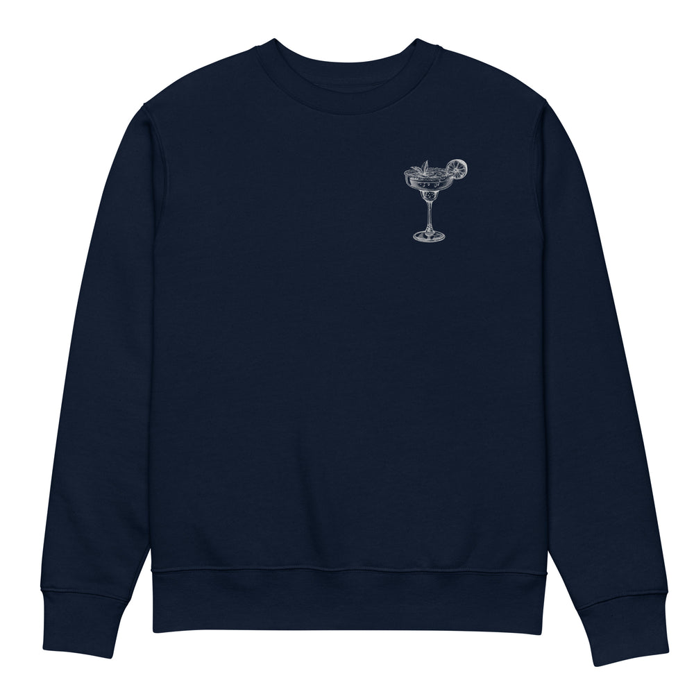 Introducing "The Mamacita Needs a Margarita Eco Sweatshirt" by Tequila & Sunrise: a navy blue unisex sweatshirt crafted from organic cotton. It features a small, white graphic of a cocktail glass with a citrus garnish on the upper left chest area, making it perfect for those who appreciate sustainable fashion.