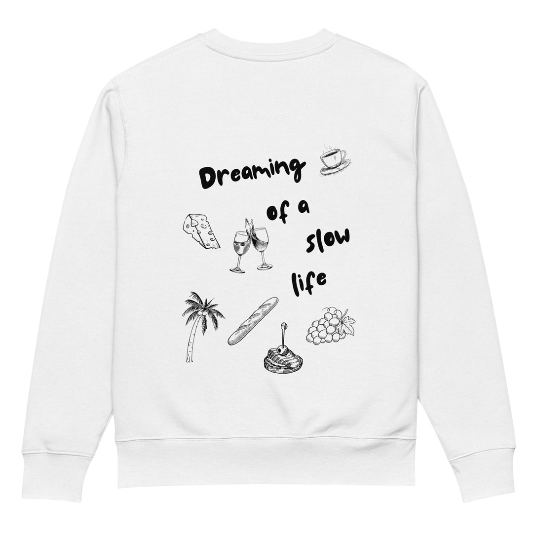 The La Vita Lenta Eco Sweatshirt by Tequila & Sunrise is a white sweatshirt made from durable organic cotton, showcasing the phrase "Dreaming of a slow life" alongside black illustrations of a coffee cup, cheese, wine glasses, palm tree, bread, steak, and grapes on a blank background.