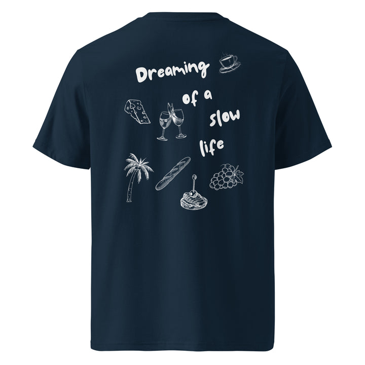 The back of The La Vita Lenta Organic T-shirt by Tequila & Sunrise showcases the phrase "Dreaming of a Slow Life" surrounded by illustrations of a teacup, game controller, wine glasses, palm tree, baguette, and grapes. Made from organic cotton, it perfectly captures the essence of slow life apparel.