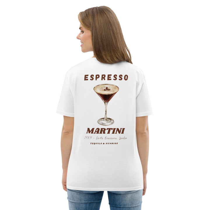 A person is wearing The Espresso Martini Organic T-shirt by Tequila & Sunrise, which is made from organic cotton and showcases an illustration of an espresso martini with the text "Espresso Martini" along with location details.