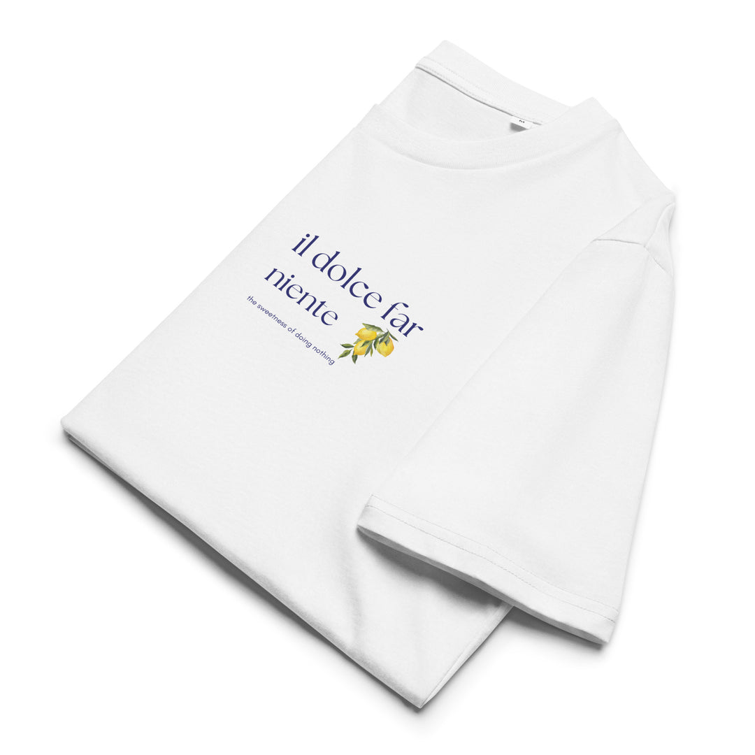 The Il Dolce Far Niente Organic T-shirt by Tequila & Sunrise is a white T-shirt made from organic cotton, adorned with the phrase "il dolce far niente" in blue and complemented by a lemon graphic on the side, beautifully embodying the essence of a Mediterranean lifestyle.