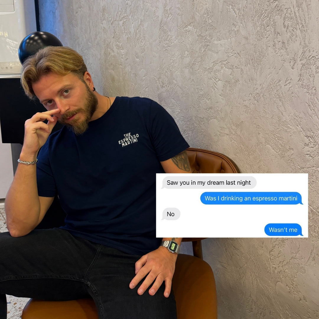 Man sitting on a chair wearing an Espresso Martini Organic T-shirt with a phone conversation about drinking an espresso martini.
