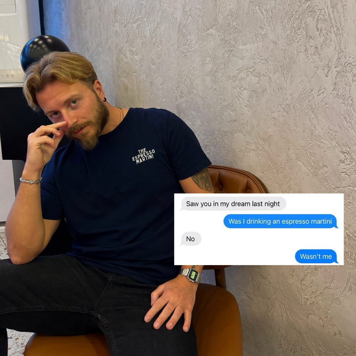 Man sitting on a chair wearing an Espresso Martini Organic T-shirt with a phone conversation about drinking an espresso martini.